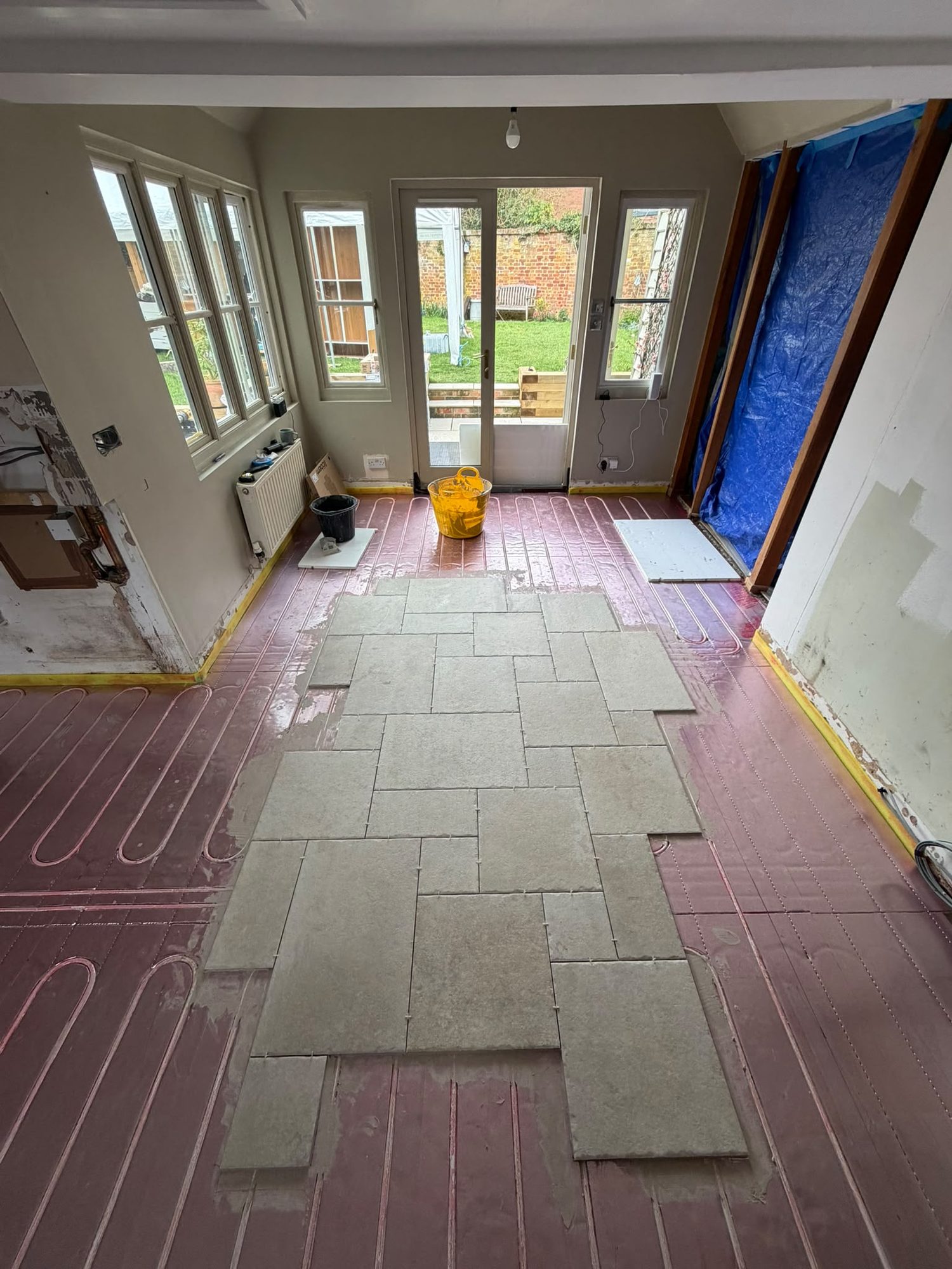 Large-format stone floor tiles being laid over underfloor heating pipework