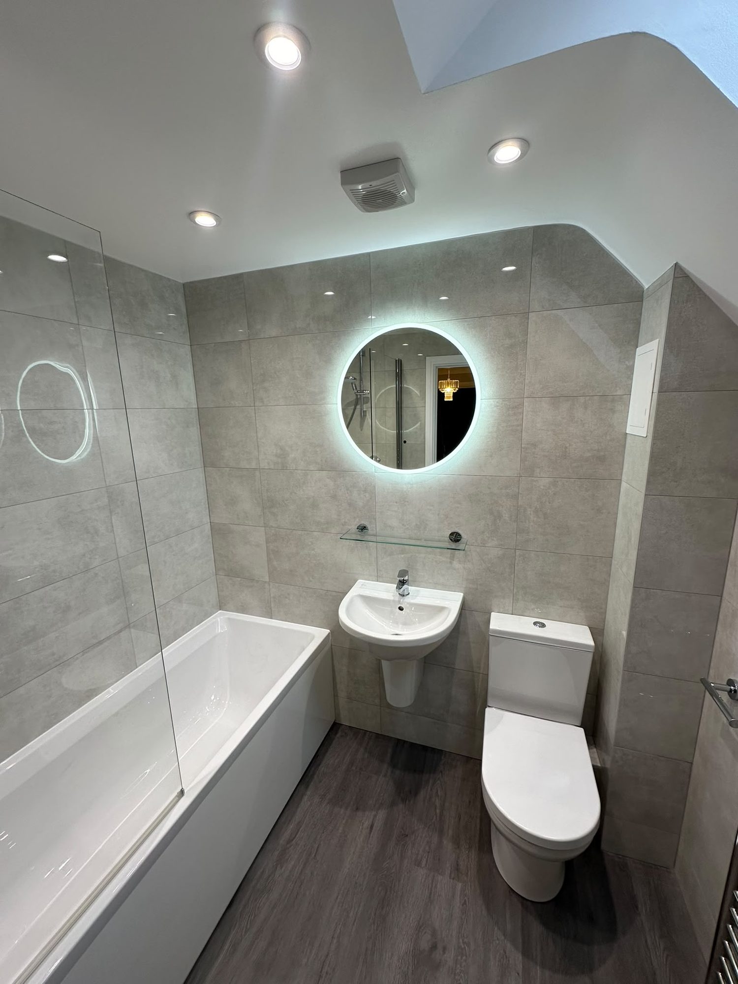 Bathroom refurbishment with bath, basin, toilet and backlit round mirror