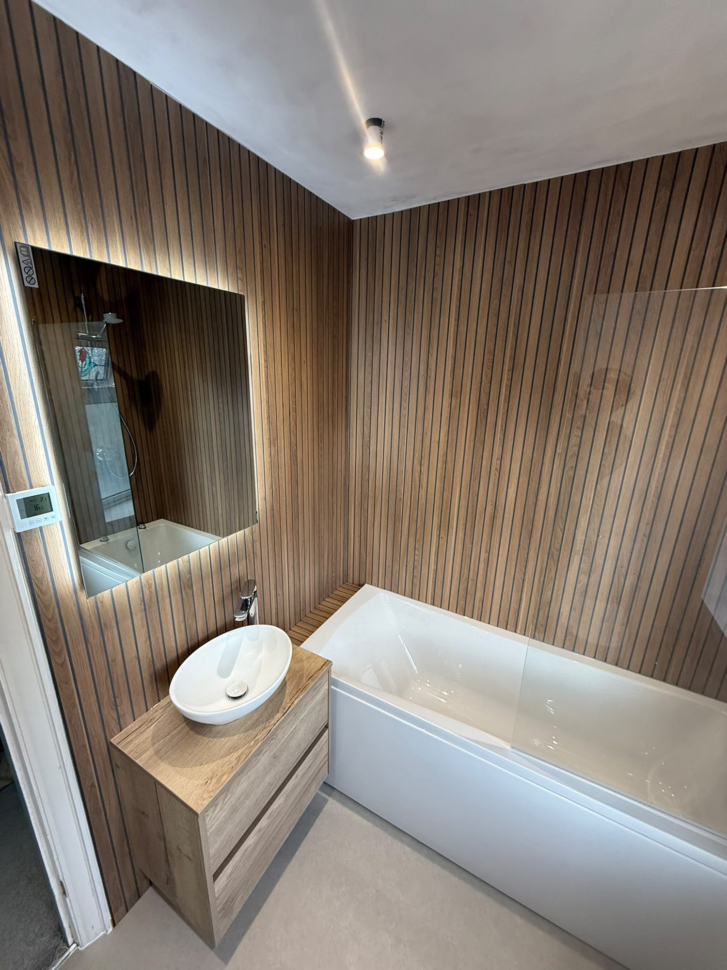 Bathroom with slat wood panelling, countertop basin and bath screen by N Monk Plumbing & Heating