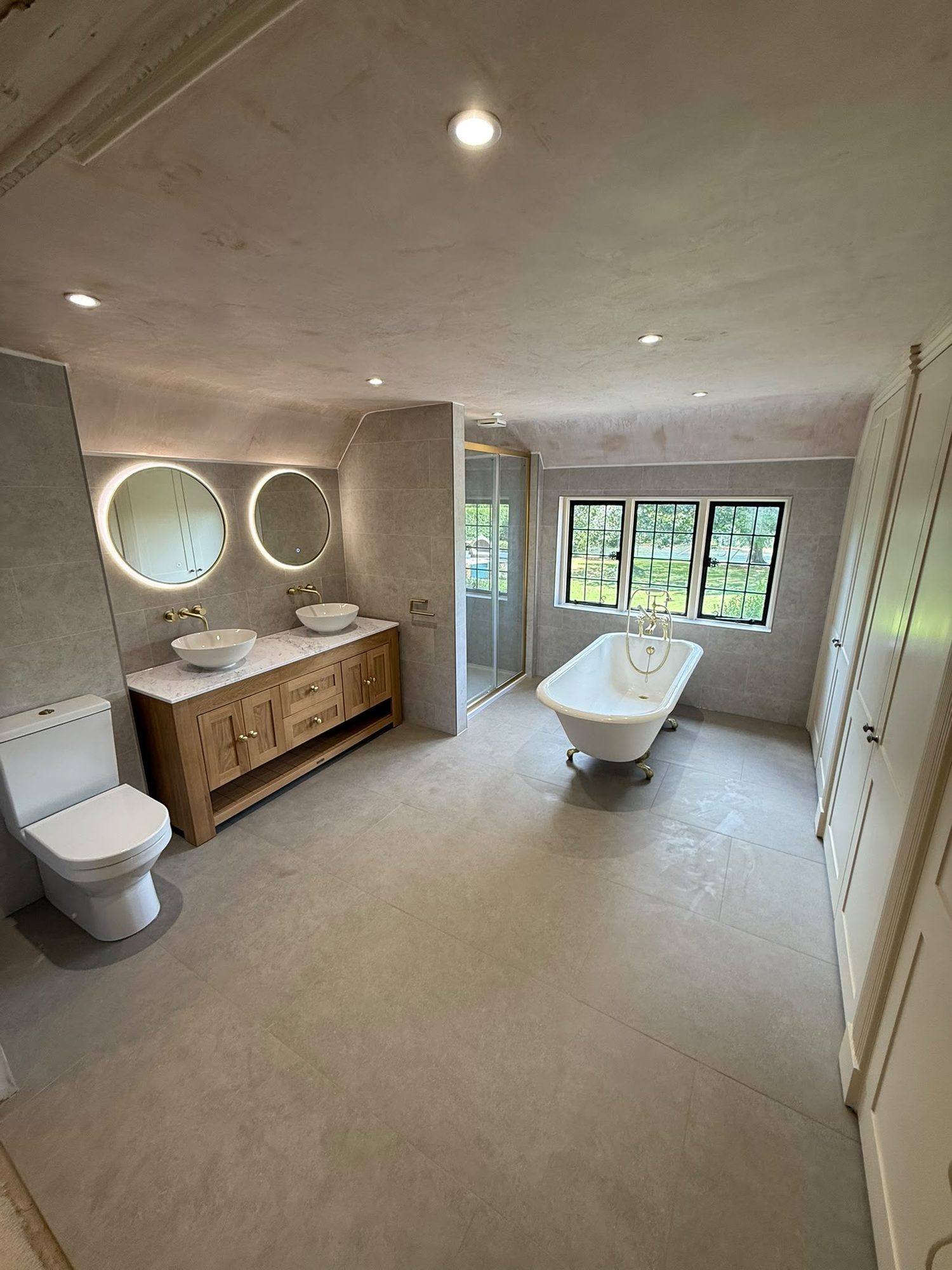 Large fitted bathroom with oak twin vanity units, round mirrors and freestanding bath