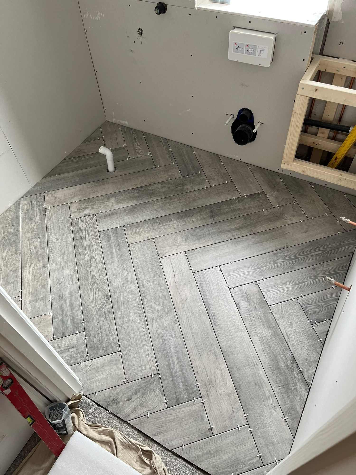 Herringbone wood-effect floor tiling laid in a bathroom during a refit