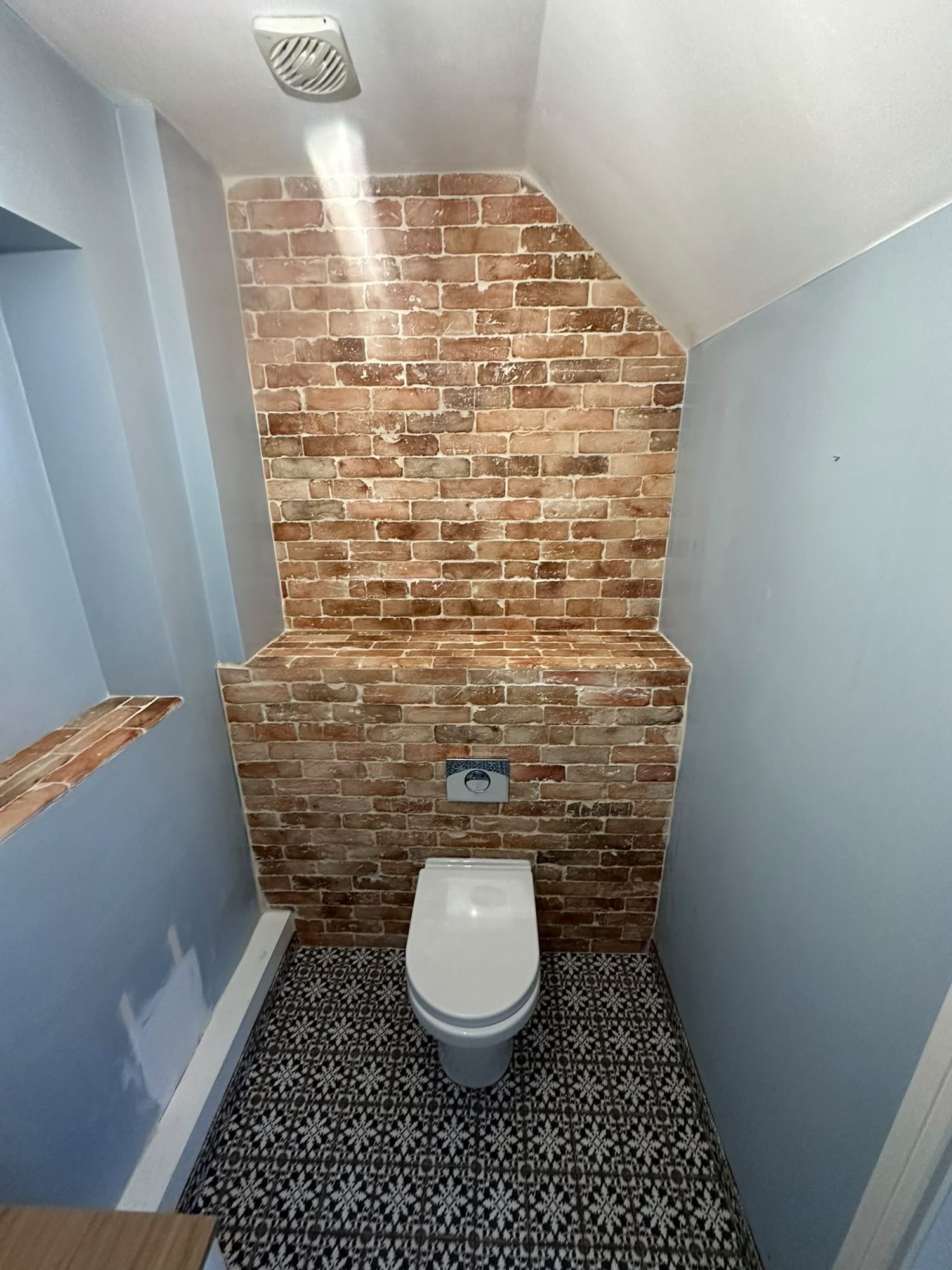 Cloakroom with brick slip feature wall, concealed cistern and patterned floor tiles