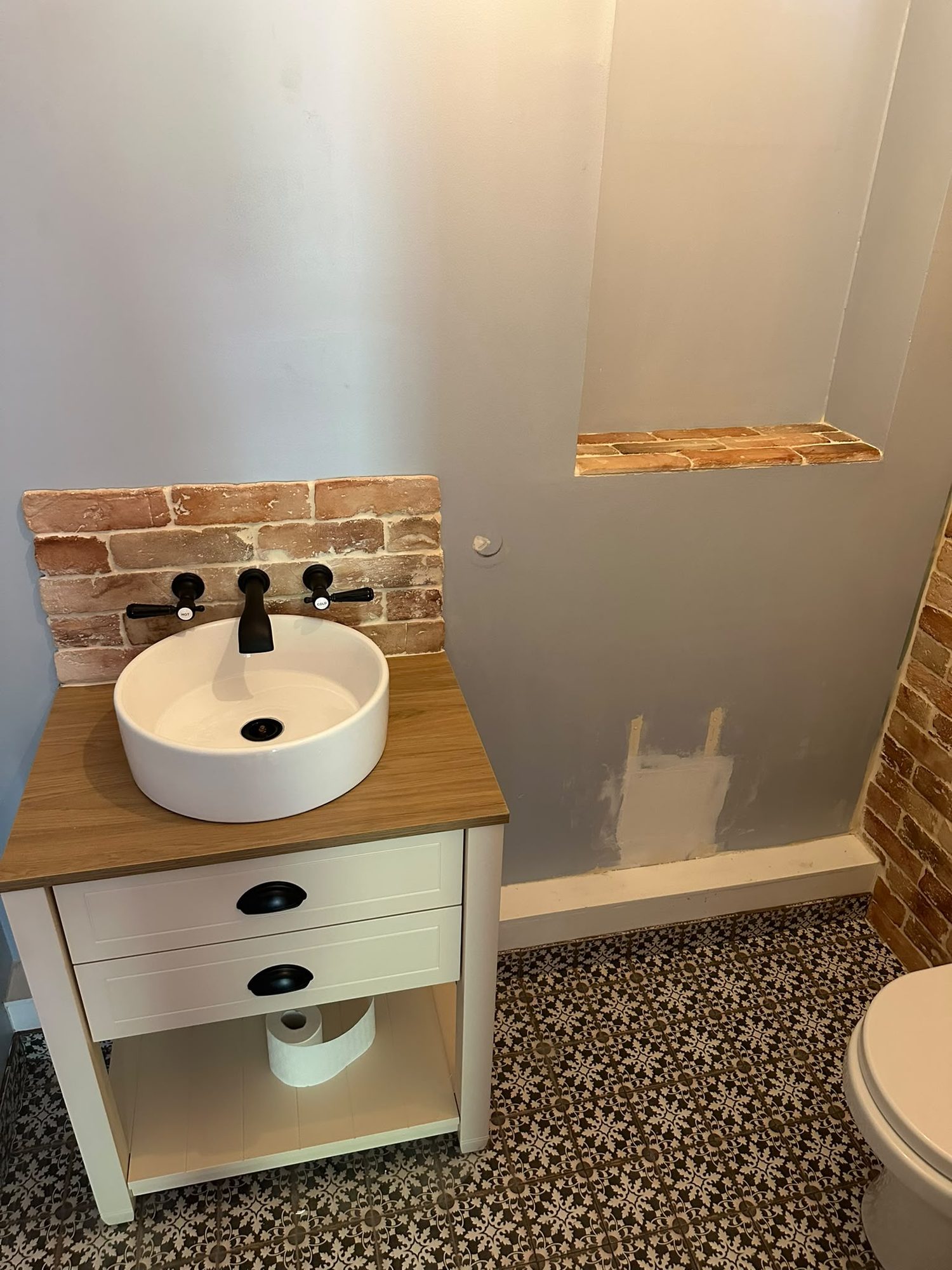 Countertop basin on an oak washstand with brick splashback and patterned floor tiles