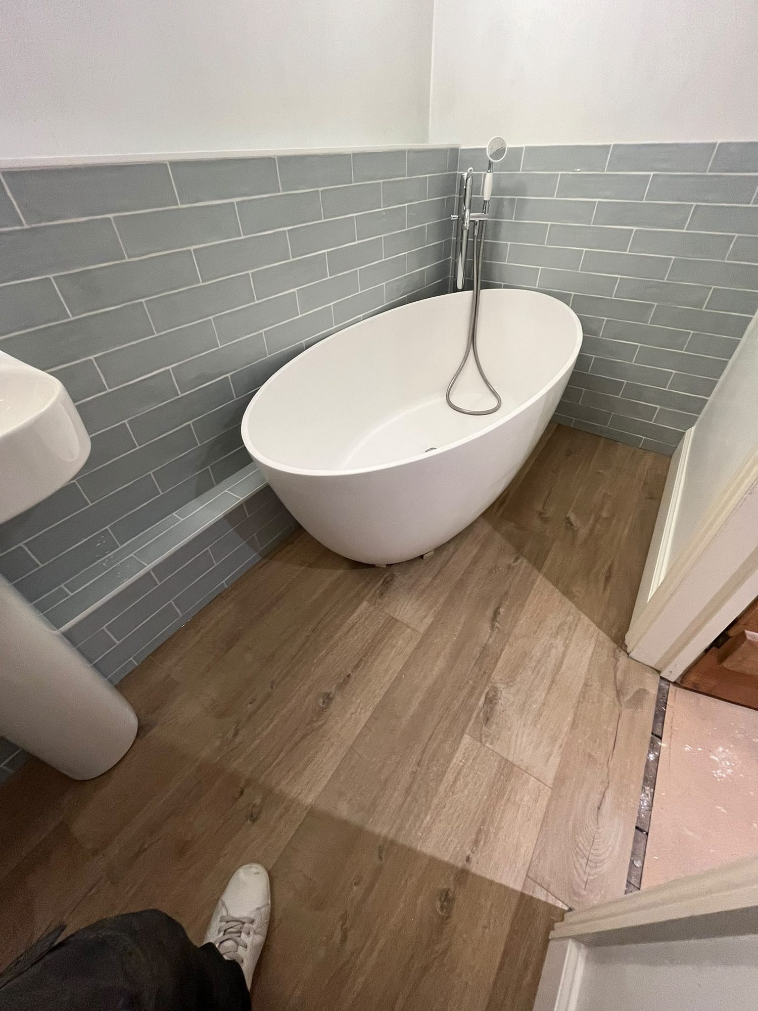 Freestanding bath with grey metro wall tiling and wood-effect flooring by N Monk Plumbing & Heating