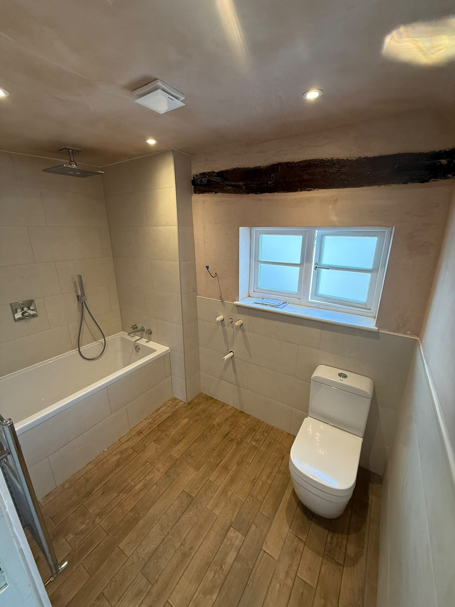 Bath with shower over, fitted beneath a window in a beamed period bathroom