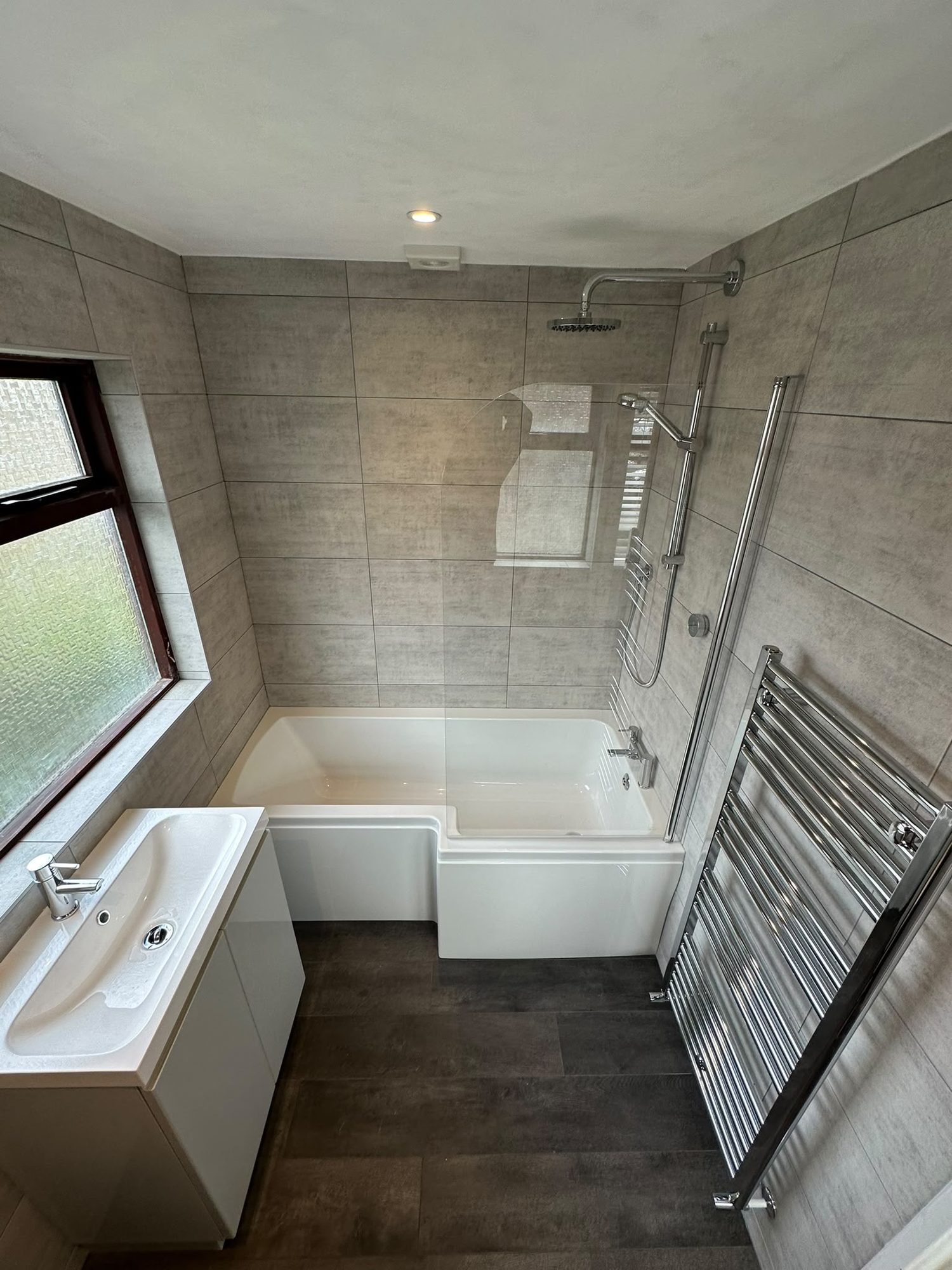 L-shaped shower bath with stone-effect wall tiling and chrome heated towel rail