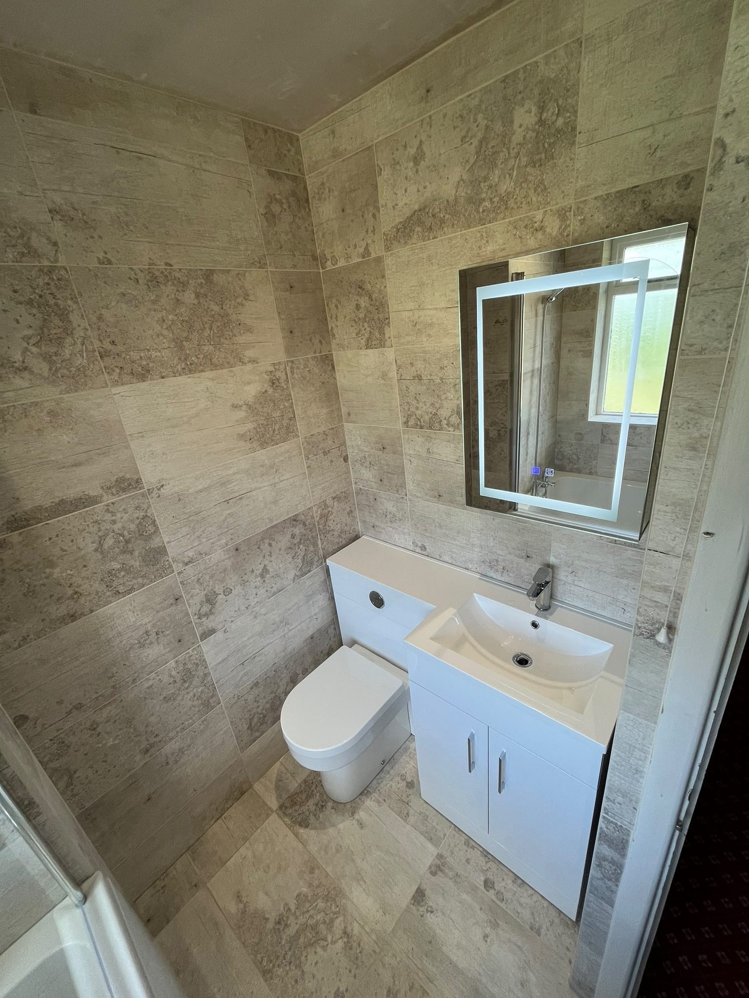 Travertine-effect tiled bathroom with white vanity unit, toilet and LED mirror