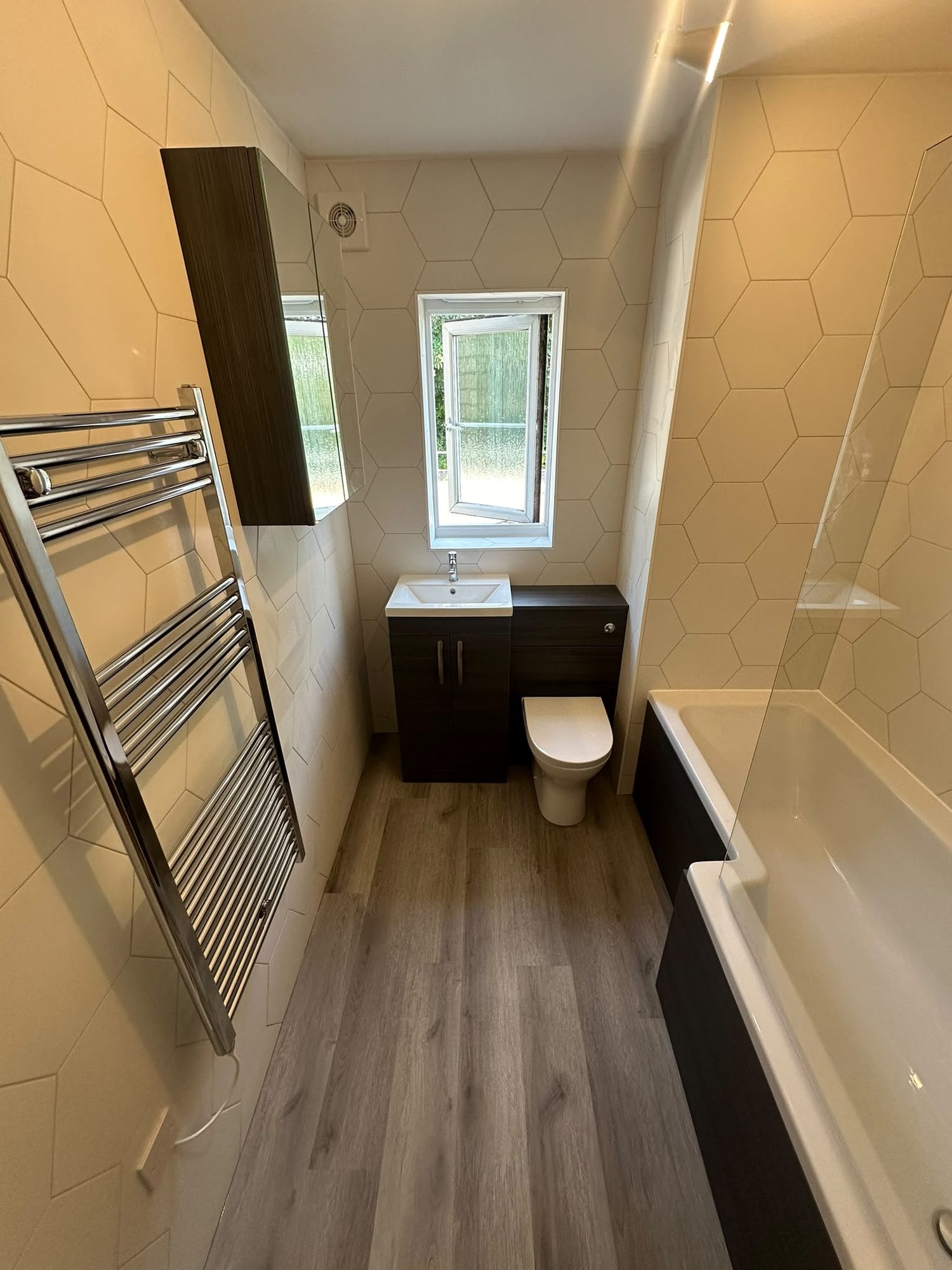 Bathroom with hexagon wall tiles, dark vanity unit, bath and heated towel rail