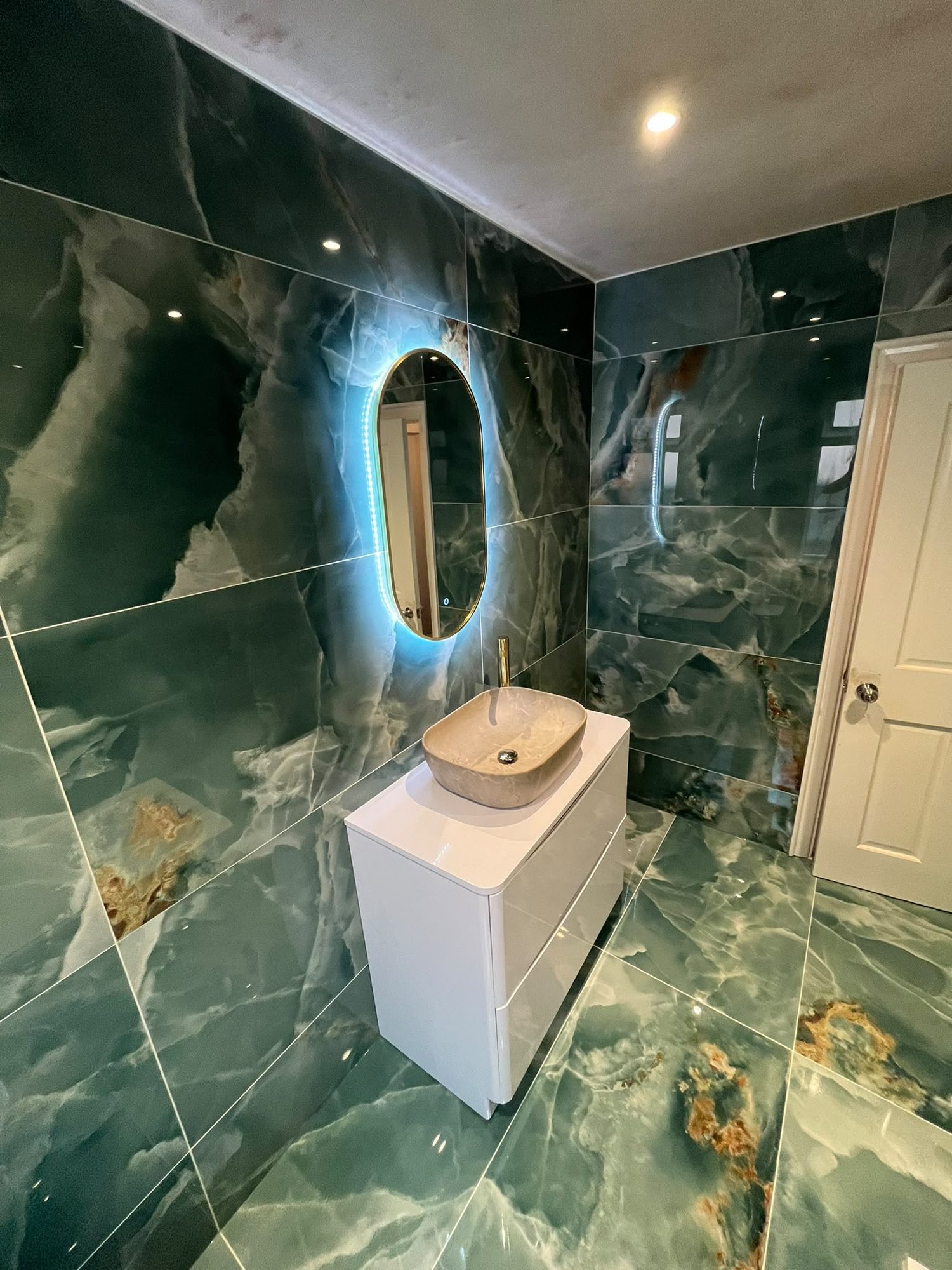 Green marble-effect bathroom with countertop basin and backlit oval mirror